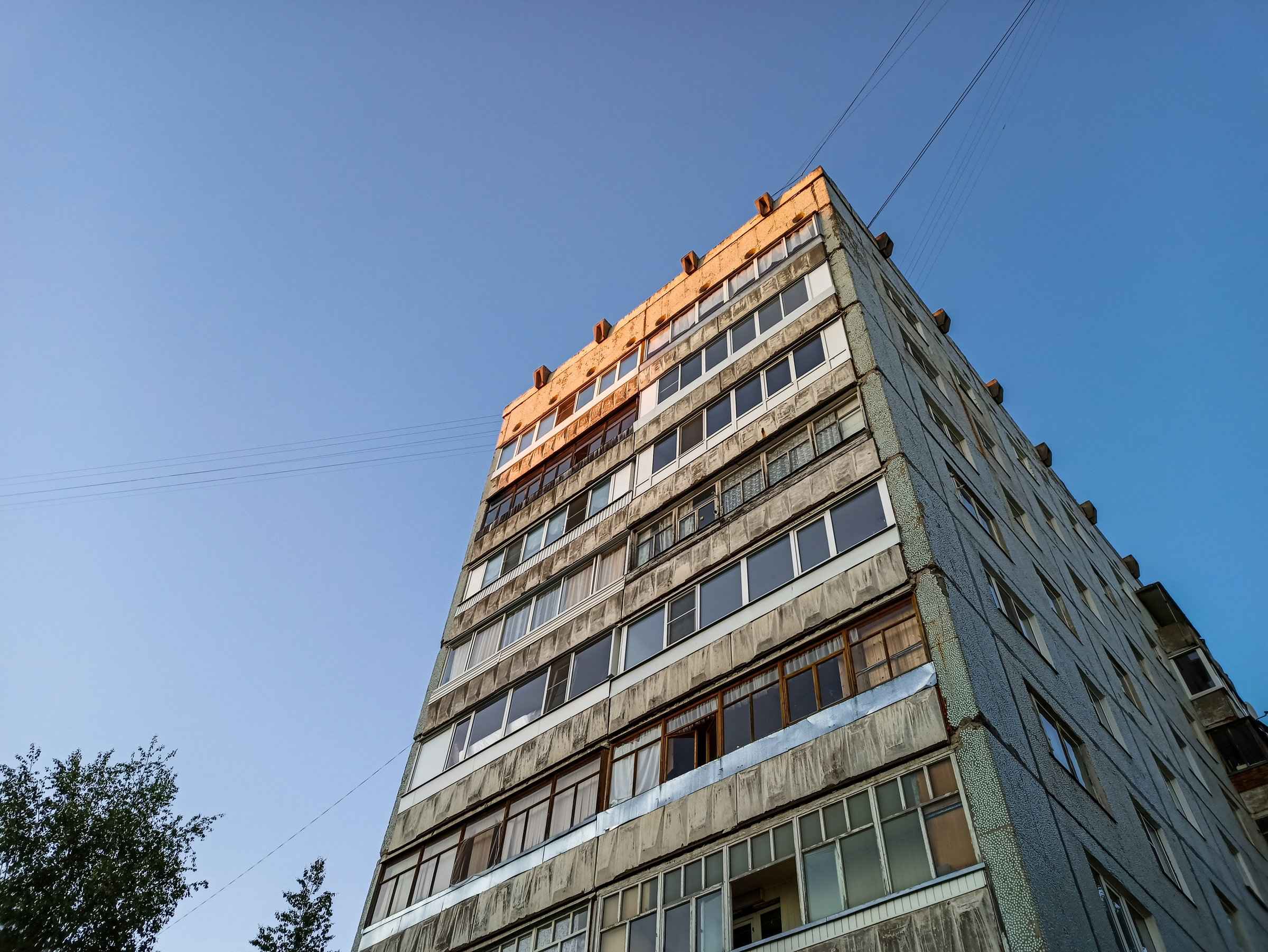 Augsta paneļu daudzdzīvokļu ēka vakara saulē uz zila debesfona